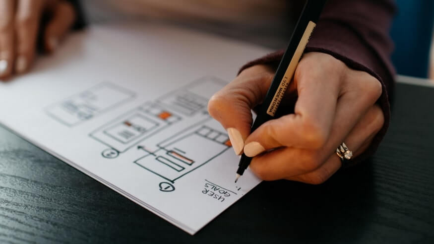 A person drawing interface architecture on paper using pencil